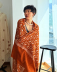 A Lady wearing an orange paisley embroidery pashmina shawl in a bright room with white curtains.